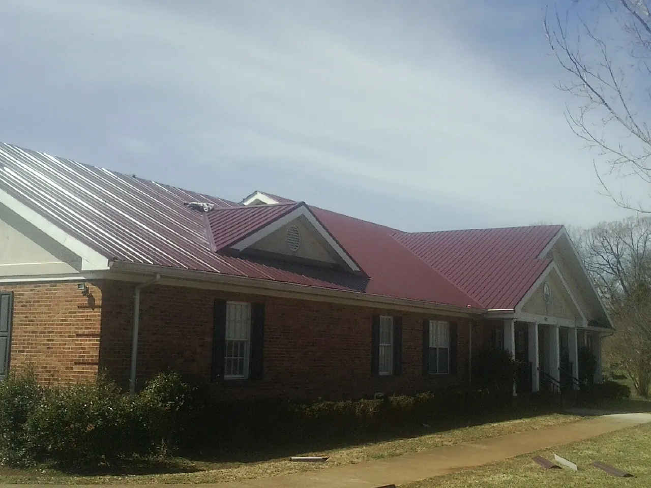 Red metal roof with gabled entries on a long brick building, from a Hail Damage Roof Repair job in Viewtown