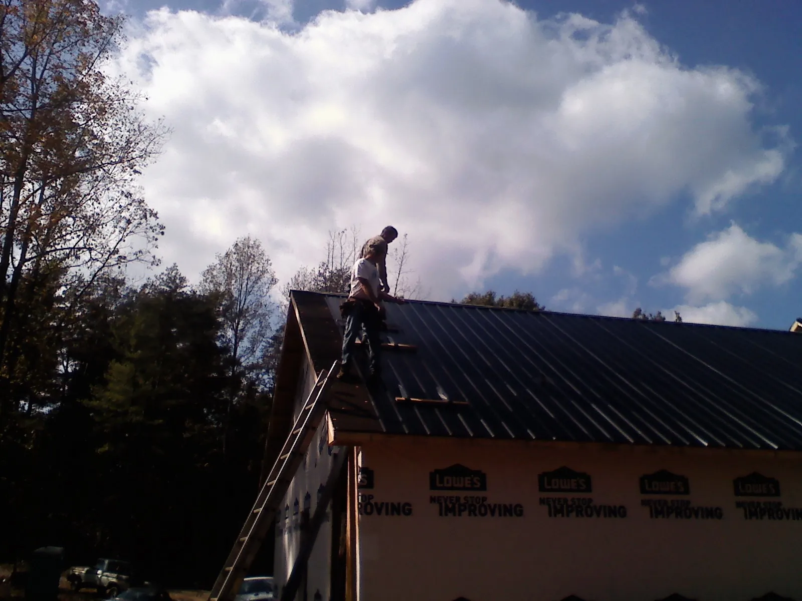 Roofer fastening dark metal panels high against a cloudy sky, from a Roof Inspection job in Viewtown